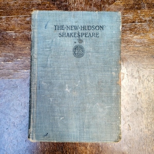 Peut inclure: Un livre relié ancien intitulé The New Hudson Shakespeare avec une couverture en tissu bleu délavé. La couverture présente un texte sombre et un logo circulaire avec les lettres WS au centre. Les bords du livre montrent des signes d'usure.