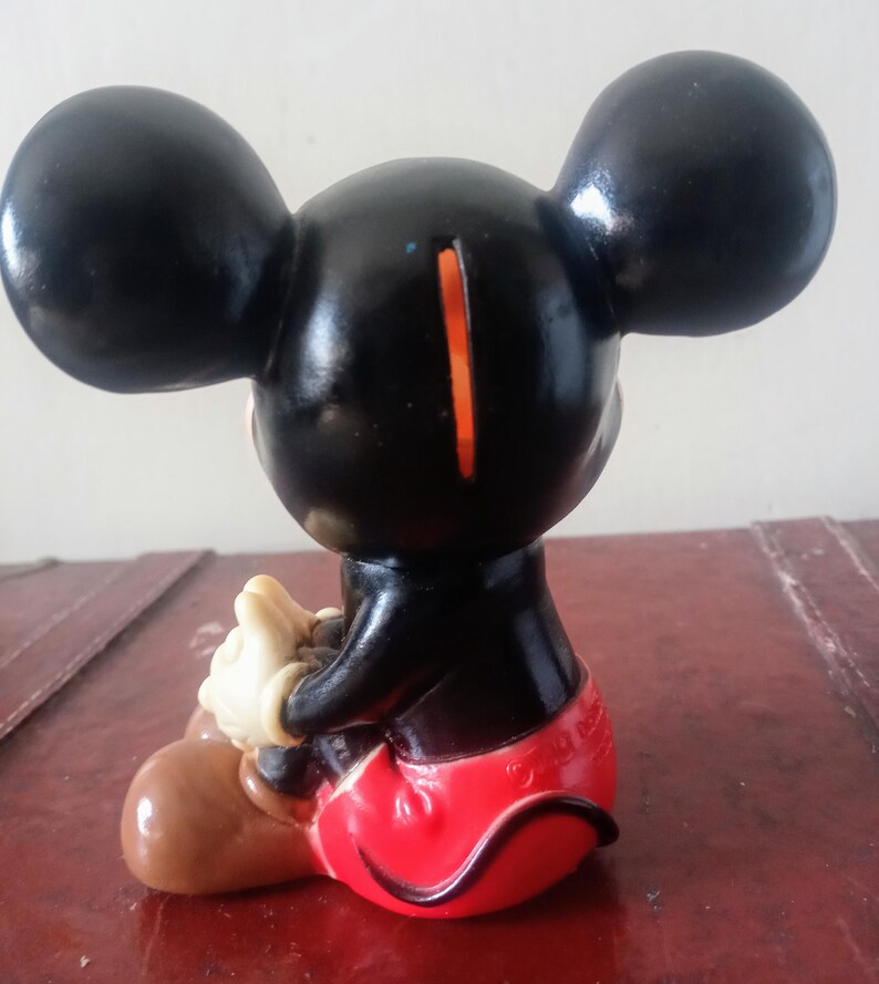 May include: A black plastic Mickey Mouse piggy bank with red shorts, brown shoes, and a slot on the back of his head.