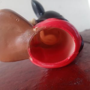 May include: A red and black plastic Mickey Mouse figurine with a brown ear. The figurine is hollow and has a hole in the bottom.