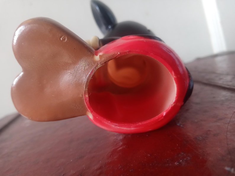 May include: A red and black plastic Mickey Mouse figurine with a brown ear. The figurine is hollow and has a hole in the bottom.