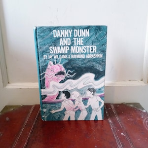 Puede incluir: Un libro de bolsillo vintage titulado "Danny Dunn y el monstruo del pantano" de Jay Williams & Raymond Abrashkin. La portada presenta un monstruo rosa con una sonrisa de dientes y tres niños que huyen de él.
