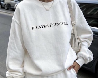 May include: White sweatshirt and matching shorts set with the text "PILATES PRINCESS" printed on the front of the sweatshirt.