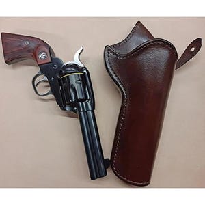 Op de afbeelding: Een zwarte single-action revolver met een donkerhouten handgreep voorzien van een zilveren embleem en een bijpassende donkerbruine lederen holster met zichtbare stiksels en een riem. Het vuurwapen heeft een metalen afwerking en een trommel met gele ring.