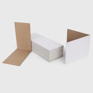 May include: A stack of white rectangular cards with a folded brown cardboard piece on the left and a folded white card on the right. The cards are neatly stacked, suggesting a stationery or packaging product.