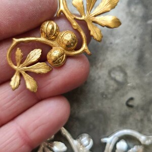 May include: Gold-toned metal embellishment with a vine design featuring leaves and round berries. The embellishment is ideal for adding a touch of elegance to crafts and home decor projects.