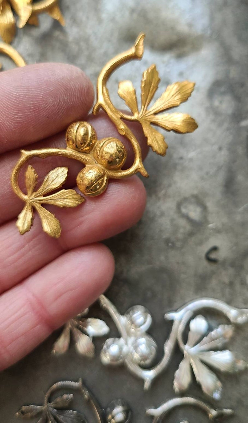 May include: Gold-toned metal embellishment with a vine design featuring leaves and round berries. The embellishment is ideal for adding a touch of elegance to crafts and home decor projects.