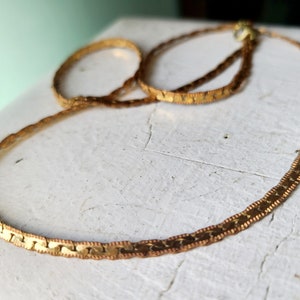 May include: A gold chain necklace with a delicate, textured design. The chain is made of small, linked pieces that create a subtle shimmer.