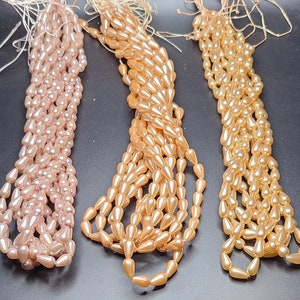 May include: Three strands of teardrop-shaped beads. The strands are made of glass beads in shades of pink, peach, and light brown.