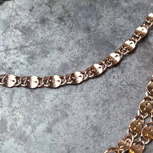 Puede incluir: Primer plano de un collar de cadena de oro rosa con eslabones ovalados. La cadena est&aacute; superpuesta sobre una superficie gris.