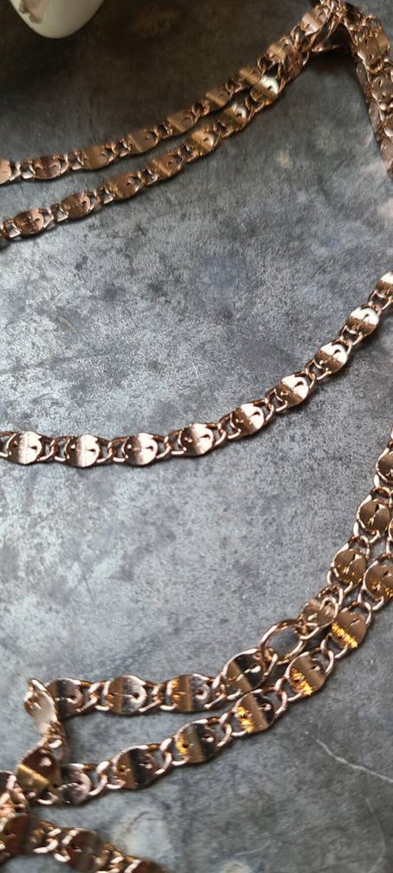 Puede incluir: Primer plano de un collar de cadena de oro rosa con eslabones ovalados. La cadena est&aacute; superpuesta sobre una superficie gris.