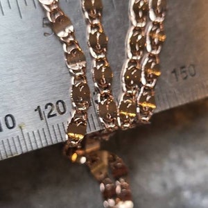 Puede incluir: Primer plano de un collar de cadena de oro con un delicado patr&oacute;n de eslabones ovalados. La cadena se mide con una regla, mostrando la longitud en pulgadas.