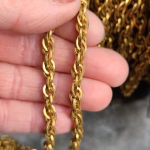 Peut inclure: Chaîne en or de type corde avec un design torsadé. La chaîne est présentée dans une main, avec plus de chaîne en arrière-plan.