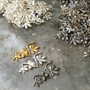 May include: A tray of metal charms in the shape of leaves and berries. The charms are in three different colours: gold, silver, and black.