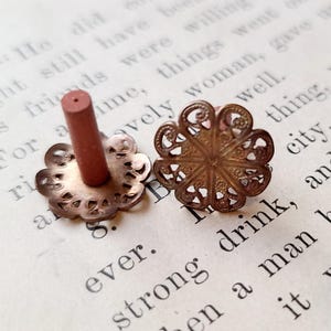 May include: Two antique gold-toned metal decorative embellishments with intricate floral designs. One embellishment has a small, round, red wooden post in the center.