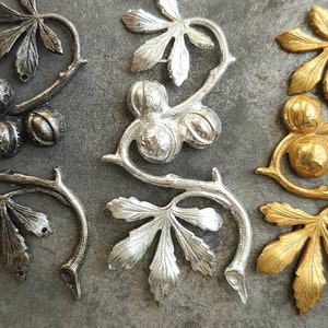 May include: Three metal decorative pieces in the shape of a vine with leaves and berries. The pieces are in black, silver, and gold.