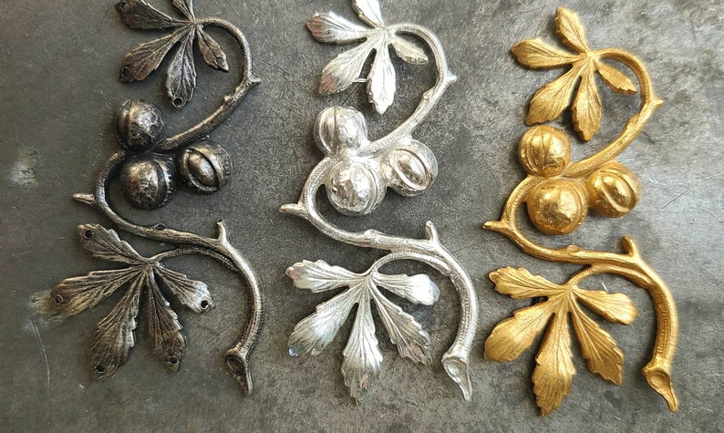 May include: Three metal decorative pieces in the shape of a vine with leaves and berries. The pieces are in black, silver, and gold.