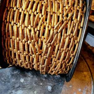 May include: A spool of gold-coloured metal chain with small, rectangular links. The chain is wound tightly around the spool, creating a dense, textured pattern.
