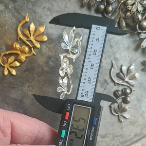 May include: A silver metal leaf design with a digital caliper measuring 6.73 cm. The caliper is black with a digital display showing the measurement in millimetres and inches.