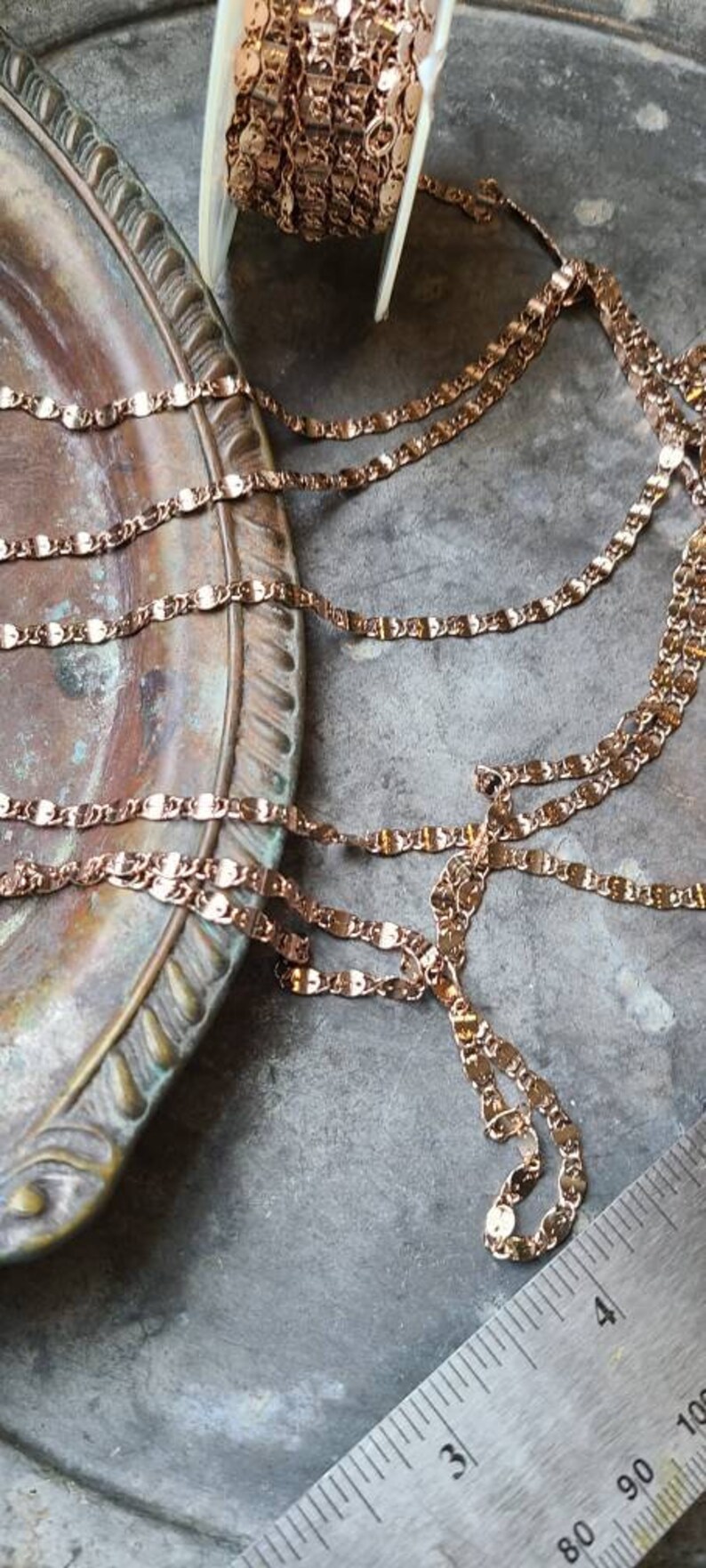 Puede incluir: Un carrete de gal&oacute;n de cadena de oro rosa con un dise&ntilde;o ondulado en forma ovalada. La cadena se muestra en una bandeja de color cobre con una regla en la esquina inferior derecha.