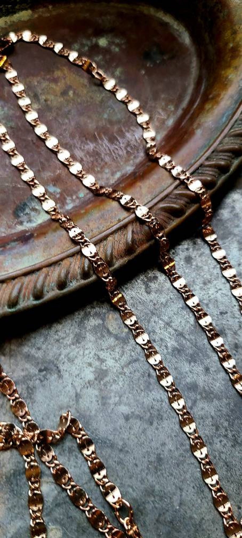 Puede incluir: Dos cadenas de oro con un patr&oacute;n ovalado enlazado yacen sobre una superficie marr&oacute;n texturizada. Las cadenas est&aacute;n hechas de un metal brillante y tienen un dise&ntilde;o cl&aacute;sico.