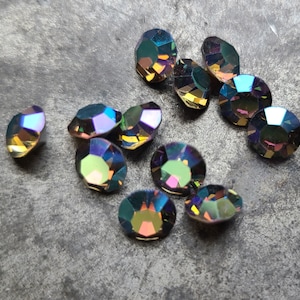 May include: Assortment of iridescent, faceted, round rhinestones in various shades of purple, blue, green, and gold.
