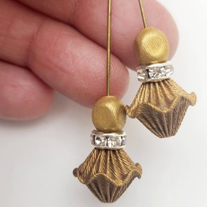 May include: A pair of gold-toned earrings with a dangling, textured, flower-shaped design. Each earring features a small, round bead and a row of clear rhinestones.