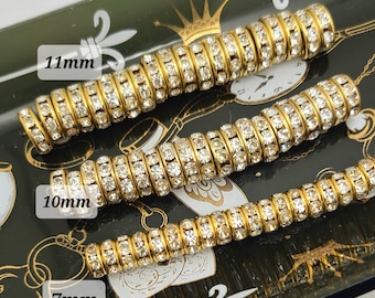 May include: Three gold-toned rhinestone bead strands, 7mm, 10mm, and 11mm in diameter, are displayed on a black decorative tray with gold accents. The beads are arranged in a row, showcasing their sparkling details.