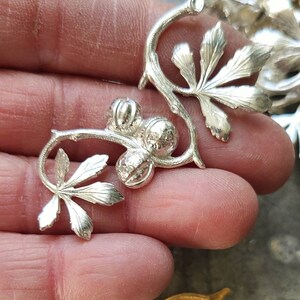 May include: A silver metal floral design with three round balls and leaves. The design is intricate and detailed.