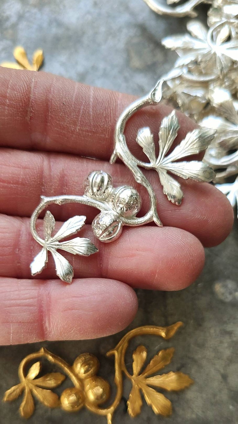 May include: A silver metal floral design with three round balls and leaves. The design is intricate and detailed.