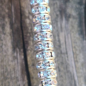 May include: A silver-toned, long, thin, decorative piece with a row of clear, sparkly rhinestones.