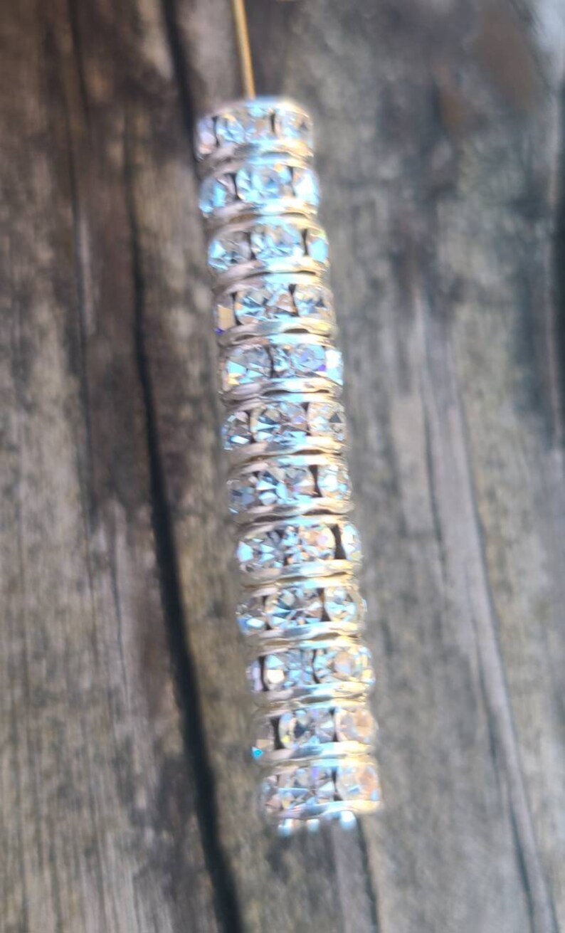 May include: A silver-toned, long, thin, decorative piece with a row of clear, sparkly rhinestones.