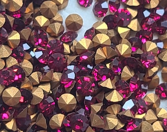 May include: A close-up image of a large quantity of small, faceted, dark red rhinestones and gold-toned metal settings. The rhinestones and settings are scattered randomly.