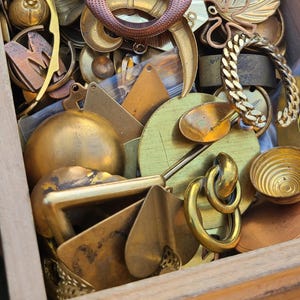 May include: A collection of vintage brass and gold-toned metal trinkets and jewelry pieces, including a butterfly charm, a chain, and a variety of decorative pieces.