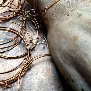 May include: A pile of gold-colored metal hoops with a hook closure. The hoops are arranged in a circular pattern on a textured surface.