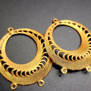 May include: Two gold-toned metal earring findings with intricate circular designs. Each finding has a loop at the top and three small loops at the bottom.