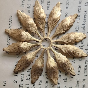 May include: A gold metal decorative piece with a circular center and 12 leaf-shaped cutouts. The piece has a textured surface and a slightly aged appearance.