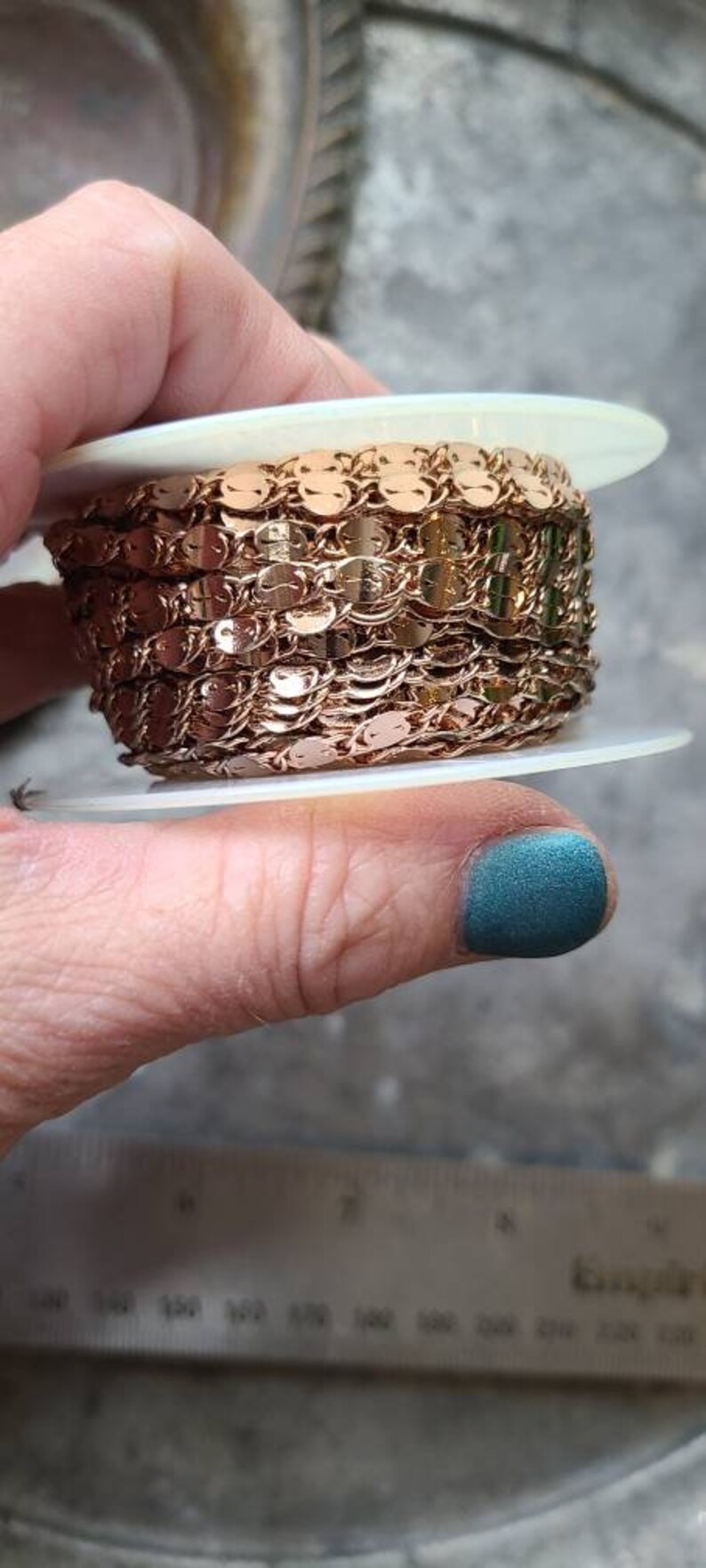 Puede incluir: Una bobina de gal&oacute;n de cadena de color oro rosa con peque&ntilde;as lentejuelas redondas. La cadena est&aacute; superpuesta en la bobina, creando un efecto decorativo.