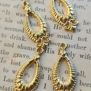 May include: Three gold-toned metal teardrop-shaped charms with intricate designs. Each charm has a loop at the top for attaching to a necklace or bracelet.