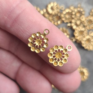 May include: Two gold-toned metal charms with a circular, openwork design and a small loop at the top. The charms are approximately 2.5 cm in diameter.