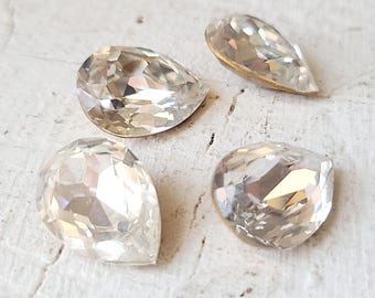 May include: Four clear pear-shaped glass rhinestones on a white background.