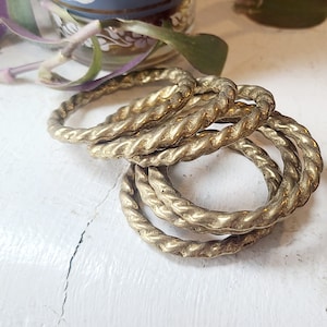 May include: A set of five gold-toned, twisted metal bangles. The bangles are stacked on top of each other, creating a decorative and unique look.