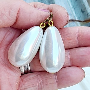 May include: A pair of teardrop-shaped pearl earrings with gold-toned hooks. The pearls are a creamy white color and have a smooth, glossy finish.