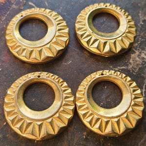May include: Four gold-colored metal rings with a geometric design. Each ring has a circular opening in the center.