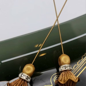 May include: Two gold tassel embellishments with a row of clear rhinestones. The tassels are attached to thin gold wires.