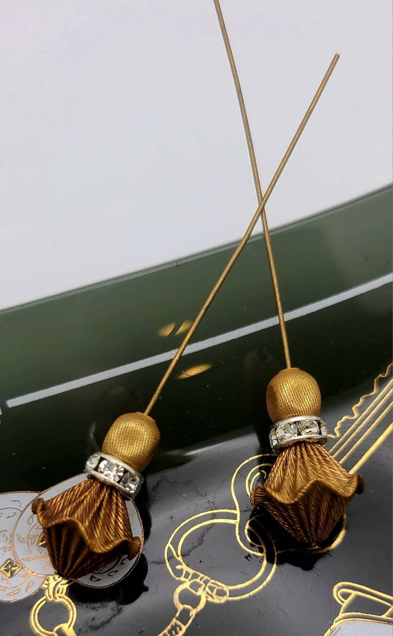 May include: Two gold tassel embellishments with a row of clear rhinestones. The tassels are attached to thin gold wires.