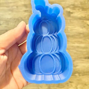 Può includere: Stampo in silicone blu a forma di pila di tre zucche. Lo stampo ha un design dettagliato con creste e uno stelo in cima.