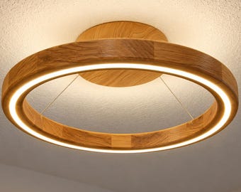 May include: A circular flush mount ceiling light fixture featuring a light brown wood grain frame with an integrated LED light strip that emits a warm glow, suspended by thin wires from a matching circular wooden base mount.