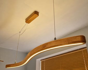 May include: A curved, light-brown wooden pendant light fixture suspended from the ceiling by thin metal wires. The fixture features a long, horizontal, wave-shaped wooden beam with an integrated LED light strip running along its underside.