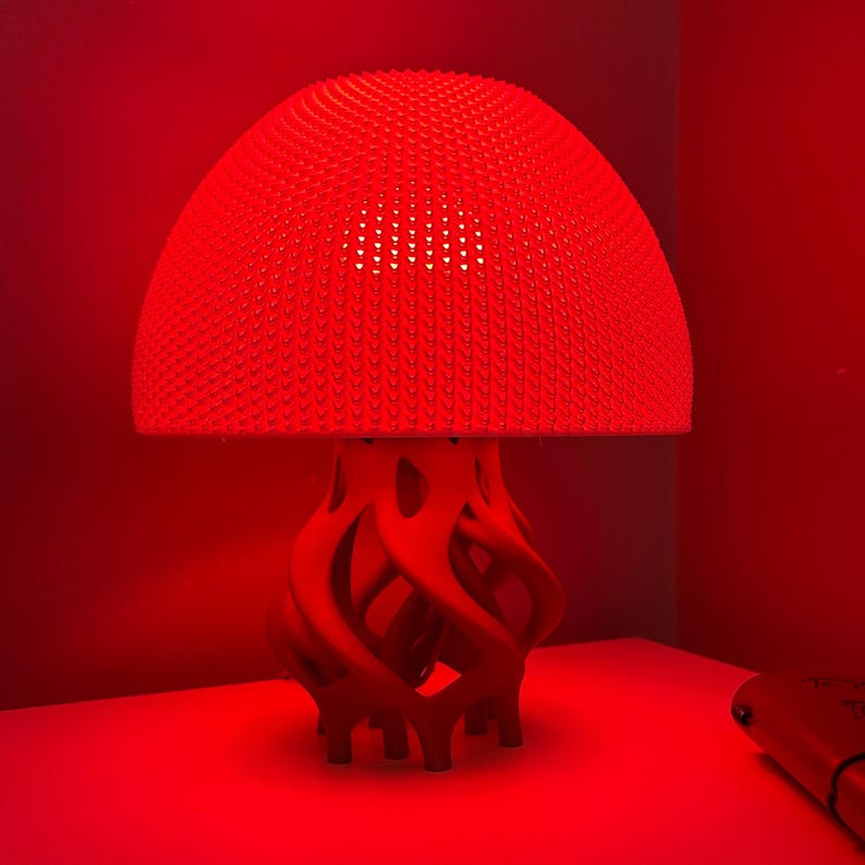 May include: A red mushroom-shaped lamp with a textured dome and a swirling, organic base. The lamp is lit, casting a red glow.