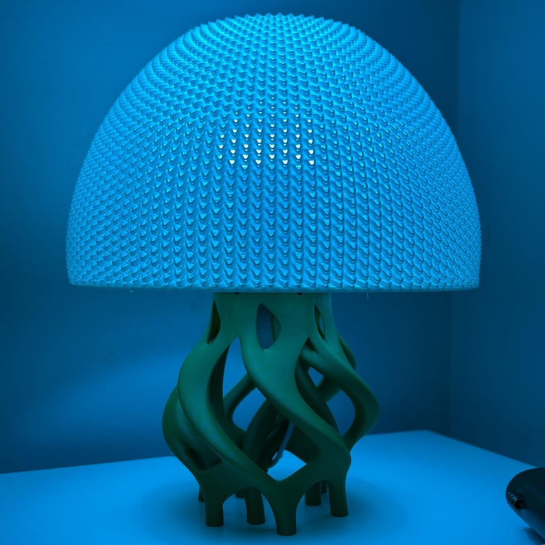 May include: A blue and green 3D printed lamp shaped like a jellyfish. The lampshade is a textured dome and the base is a swirling, organic shape.